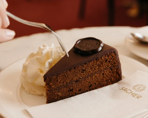 Ein Stück Original Sacher-Torte mit ungesüßtem Schlagobers auf einem Marmortisch.