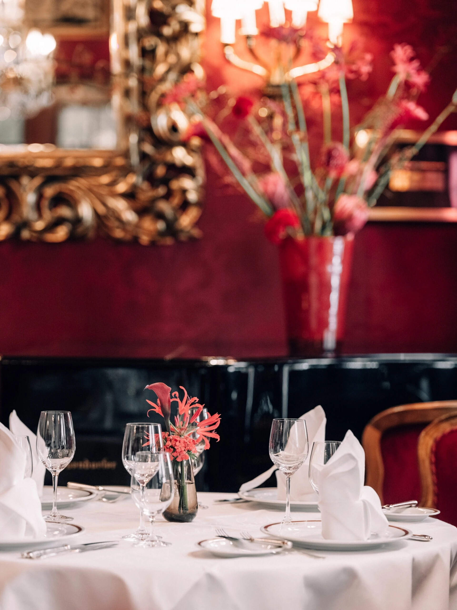 Elegant gedeckter Speisesaal des Restaurant Rote Bar im Hotel Sacher Wien mit roten Samtstühlen, Kristallleuchtern und historischen Gemälden.