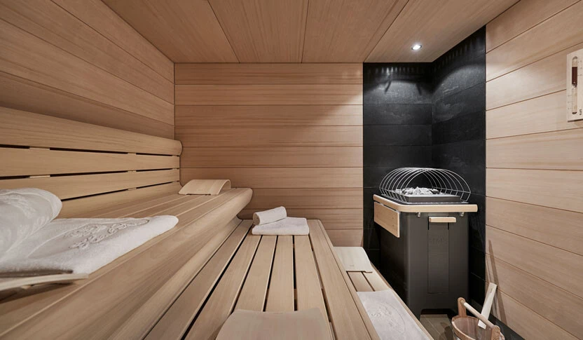 Moderne Sauna mit hellem Holzinterieur, zwei Liegebänken und stilvollem schwarzen Saunaofen in der Ecke