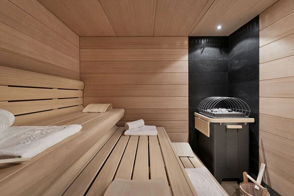 Moderne Sauna mit hellem Holzinterieur, zwei Liegebänken und stilvollem schwarzen Saunaofen in der Ecke