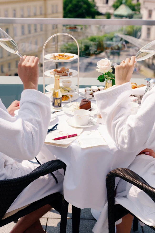Brautpaar im Bademantel stößt beim Frühstück mit Champagner auf einer Terrasse des Hotel Sacher Wien an.