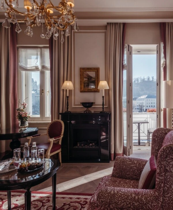 Familiensuite mit Ausblick im Hotel Sacher Salzburg, mit Schlafzimmer, Sitzbereich und eleganten roten Musterdetails
