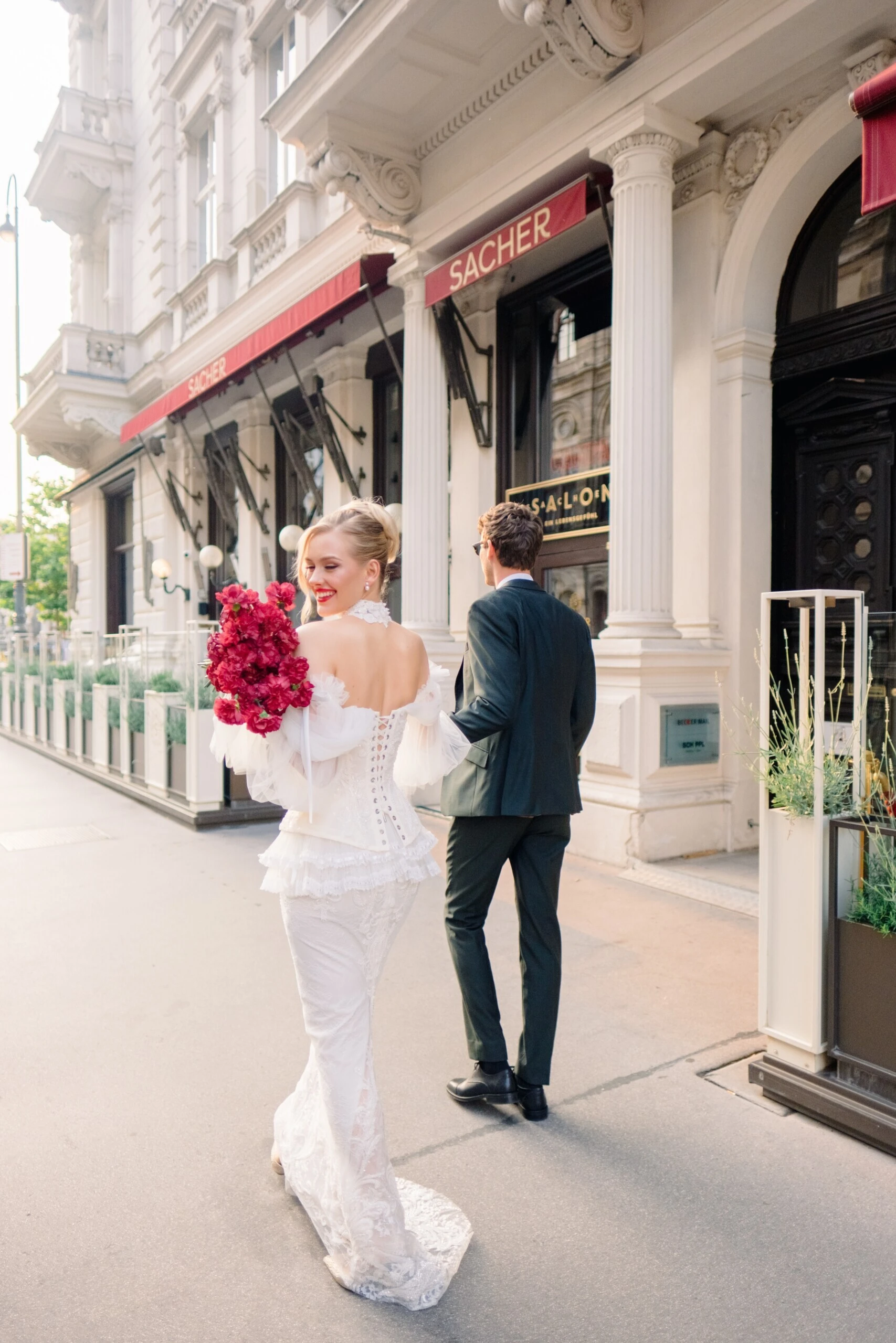 Brautpaar vor dem Hotel Sacher Wien, die Braut in einem weißen Hochzeitskleid mit pinkem Blumenstrauß
