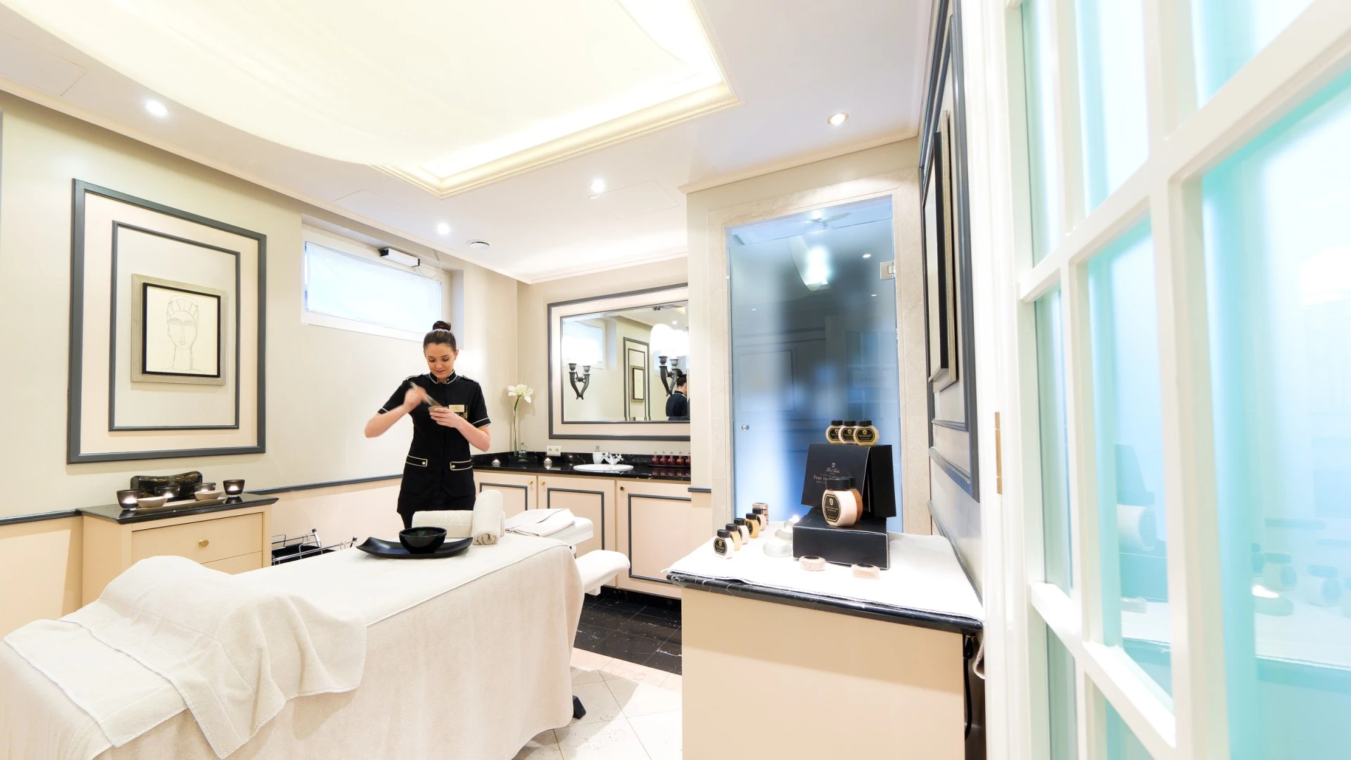 Heller, elegant gestalteter Behandlungsraum mit Massageliege, gepflegtem Interieur in Creme- und Schwarztönen