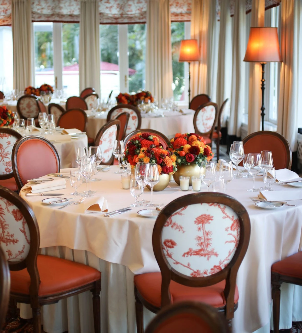 Nahaufnahme eines elegant gedeckten Tisches in einem stilvollen Restaurant mit weißer Tischdecke, feinem Glas- und Silberbesteck, im Hintergrund warme Beleuchtung und klassisch gepolsterte Stühle mit rotem Dekor.