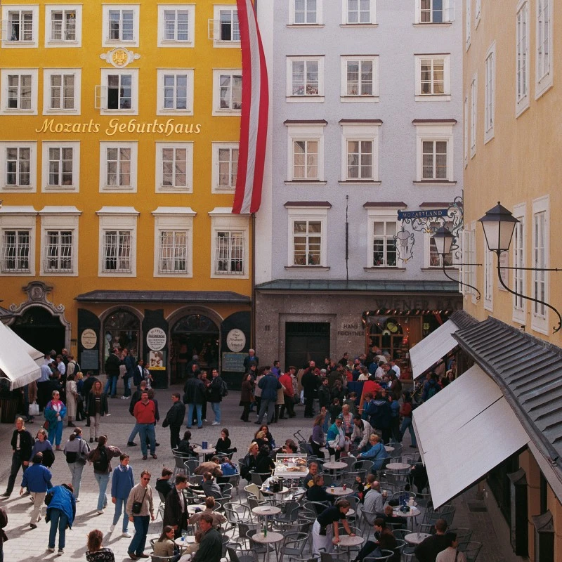 Mozarts Geburtshaus in der Getreidegasse, Salzburg, mit belebtem Platz und Straßencafé.