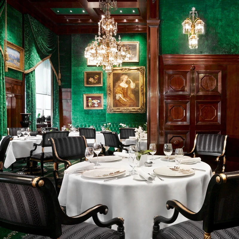 Elegantes Restaurant mit grüner Wandbespannung, Kronleuchtern und klassisch gedeckten Tischen.