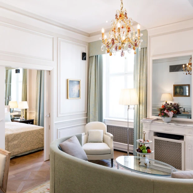 Heller Salon mit pastellgrüner Couch, Marmorkamin, Kristalllüster, frischem Obst auf dem Glastisch und Blick ins angeschlossene Schlafzimmer.