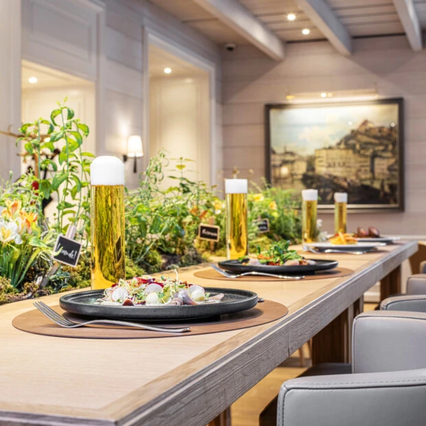 Modern gedeckter langer Holztisch mit beigen Lederstühlen in einem hellen, elegant eingerichteten Raum mit sichtbarer Holzdecke.