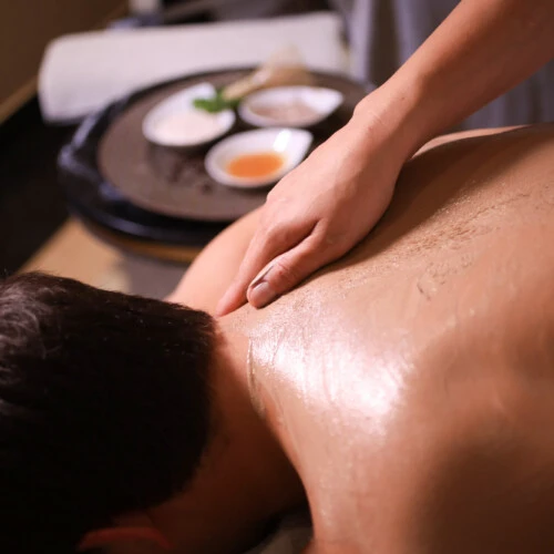 Wellnessbehandlung mit Rückenmassage, natürliche Pflegeprodukte im Hintergrund auf vorbereitetem Tablett.