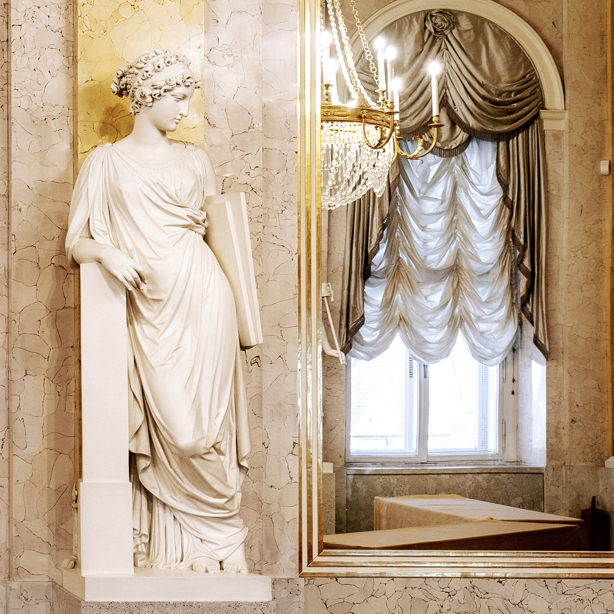 A serene marble statue of a woman with a scroll leans elegantly in the opulent Albertina Palace.