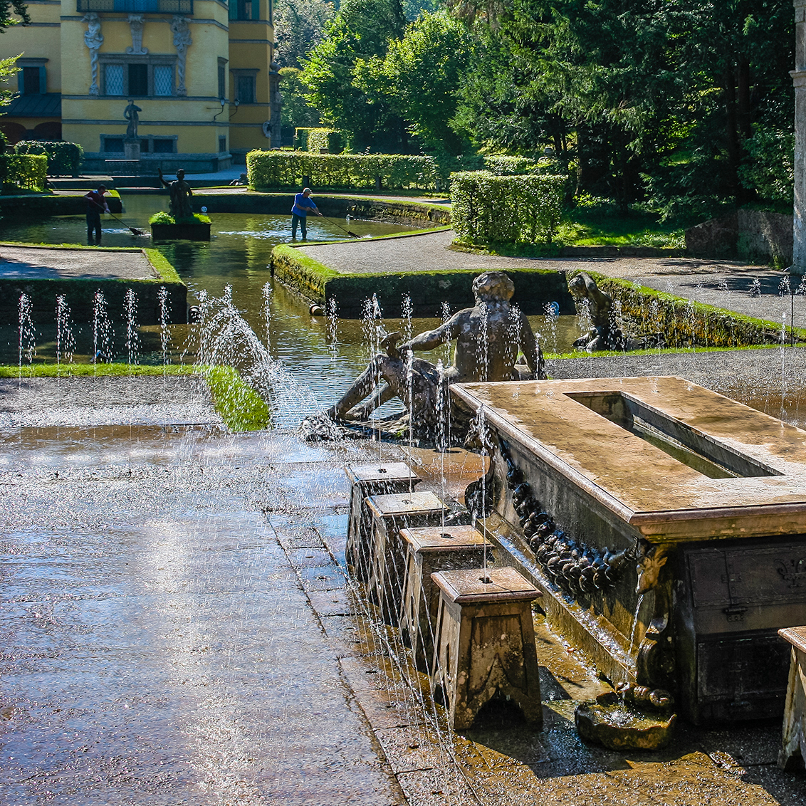 This image shows a playful trick fountain table surrounded by stools at Hellbrunn Palace in Salzburg, Austria, designed to surprise guests with hidden water jets in a beautifully manicured garden setting.