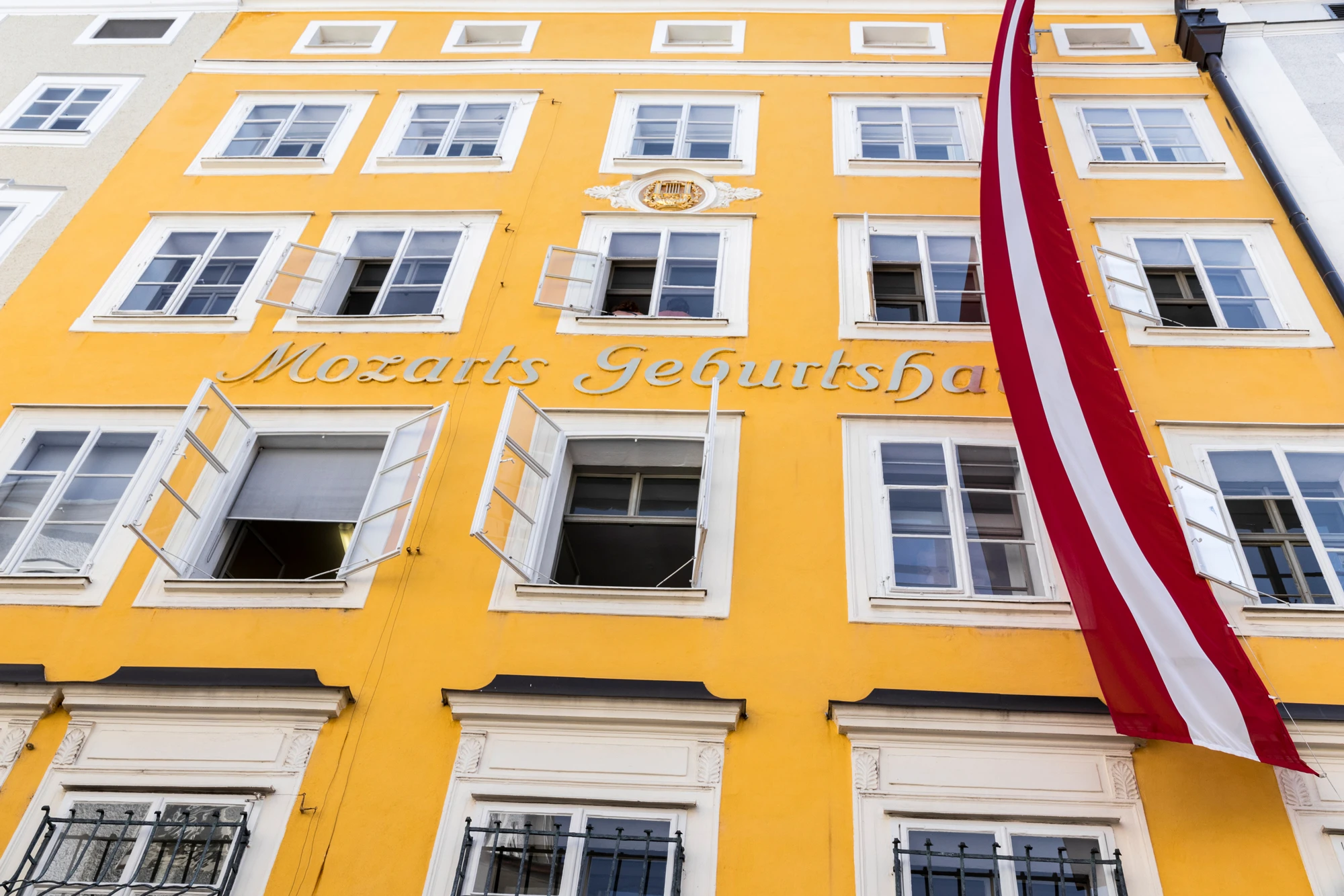 This image shows Mozart's Birthplace in Salzburg, Austria, a bright yellow historic building marked with the words 