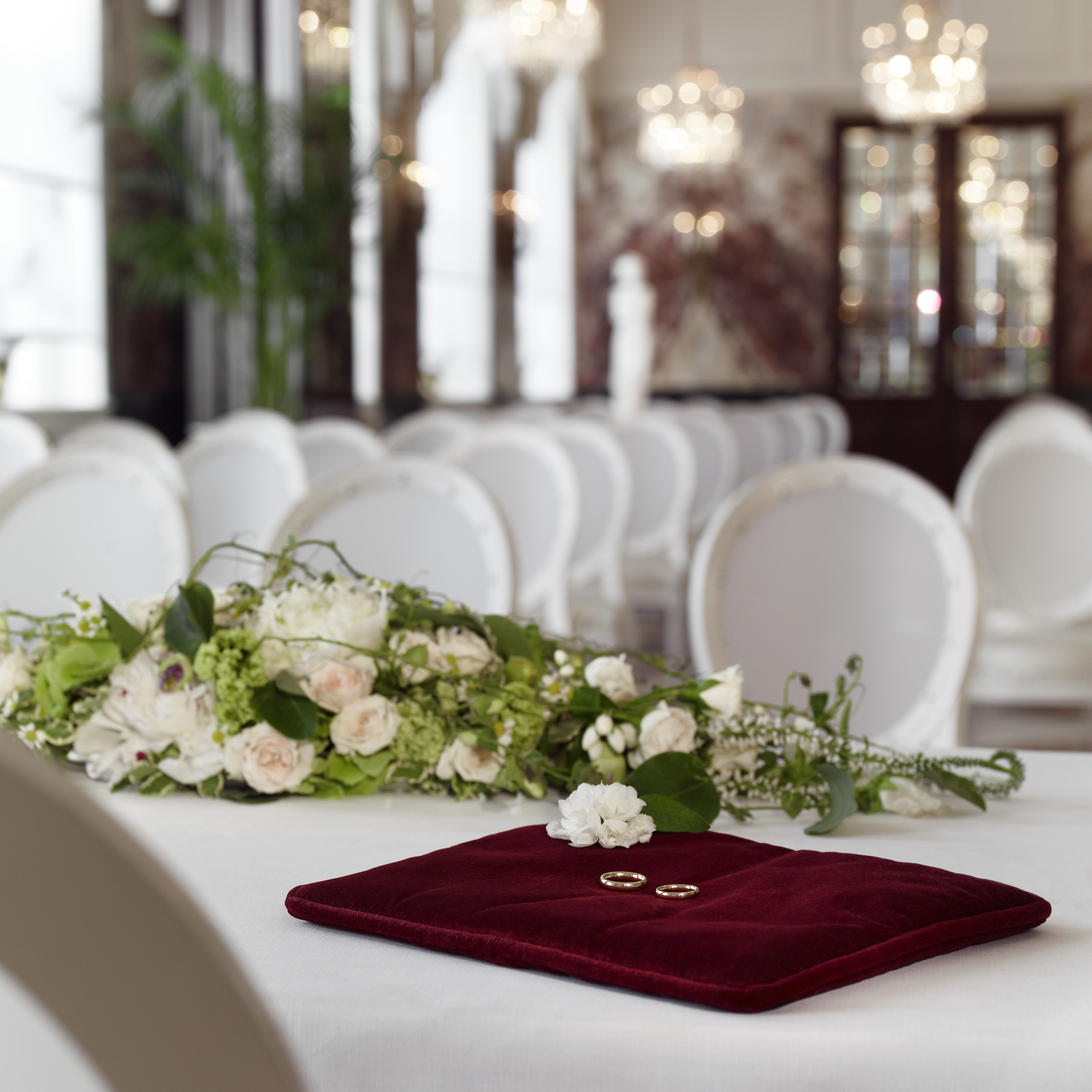 Marmorsaal - Marble Hall 4 A pair of wedding rings rest on a red velvet cushion beside a floral bouquet, set in the elegant white interior of the Marmorsaal.