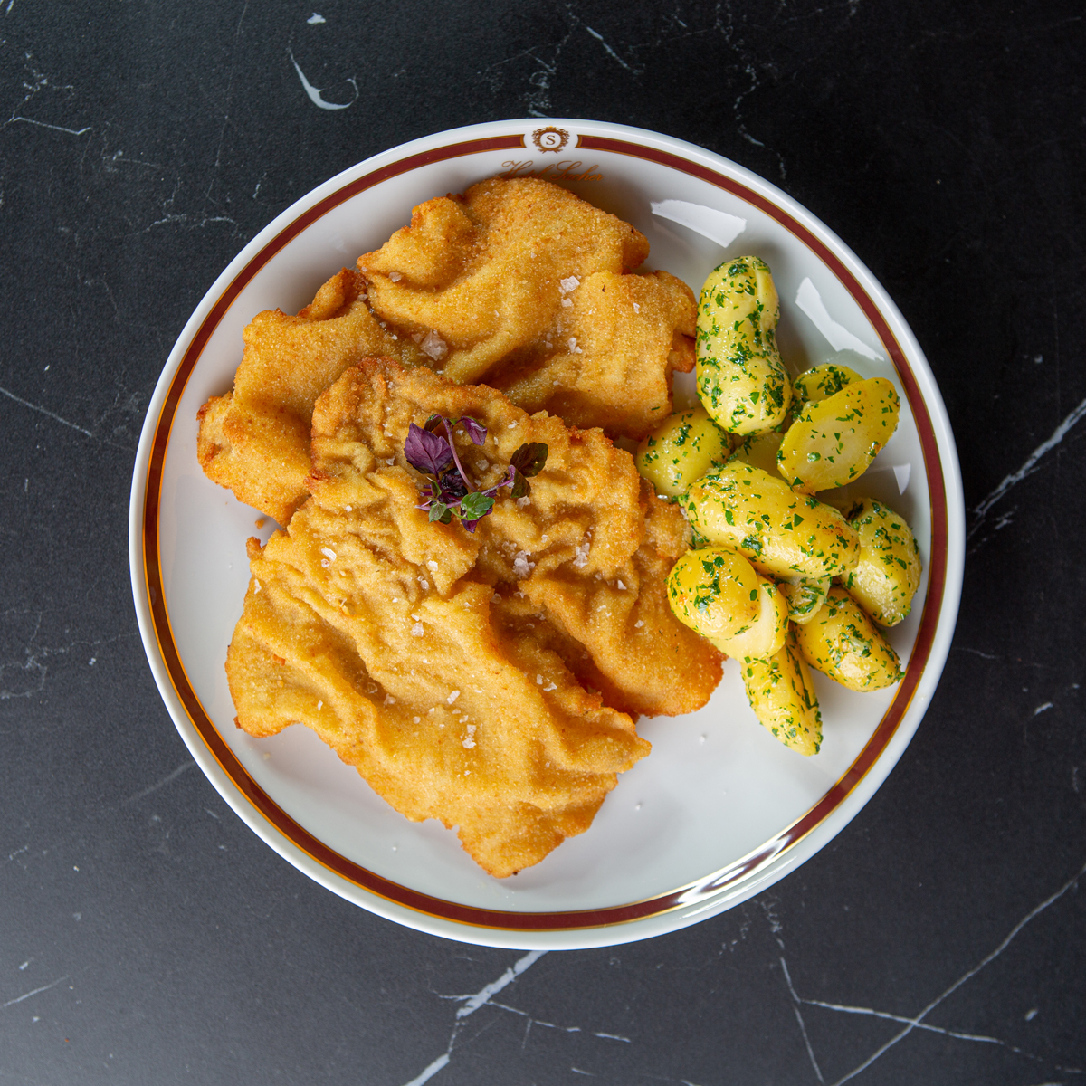sacher_wiener-schnitzel_bild A perfectly golden Wiener Schnitzel served with traditional parsley potatoes—an iconic Austrian dish presented with Hotel Sacher elegance.