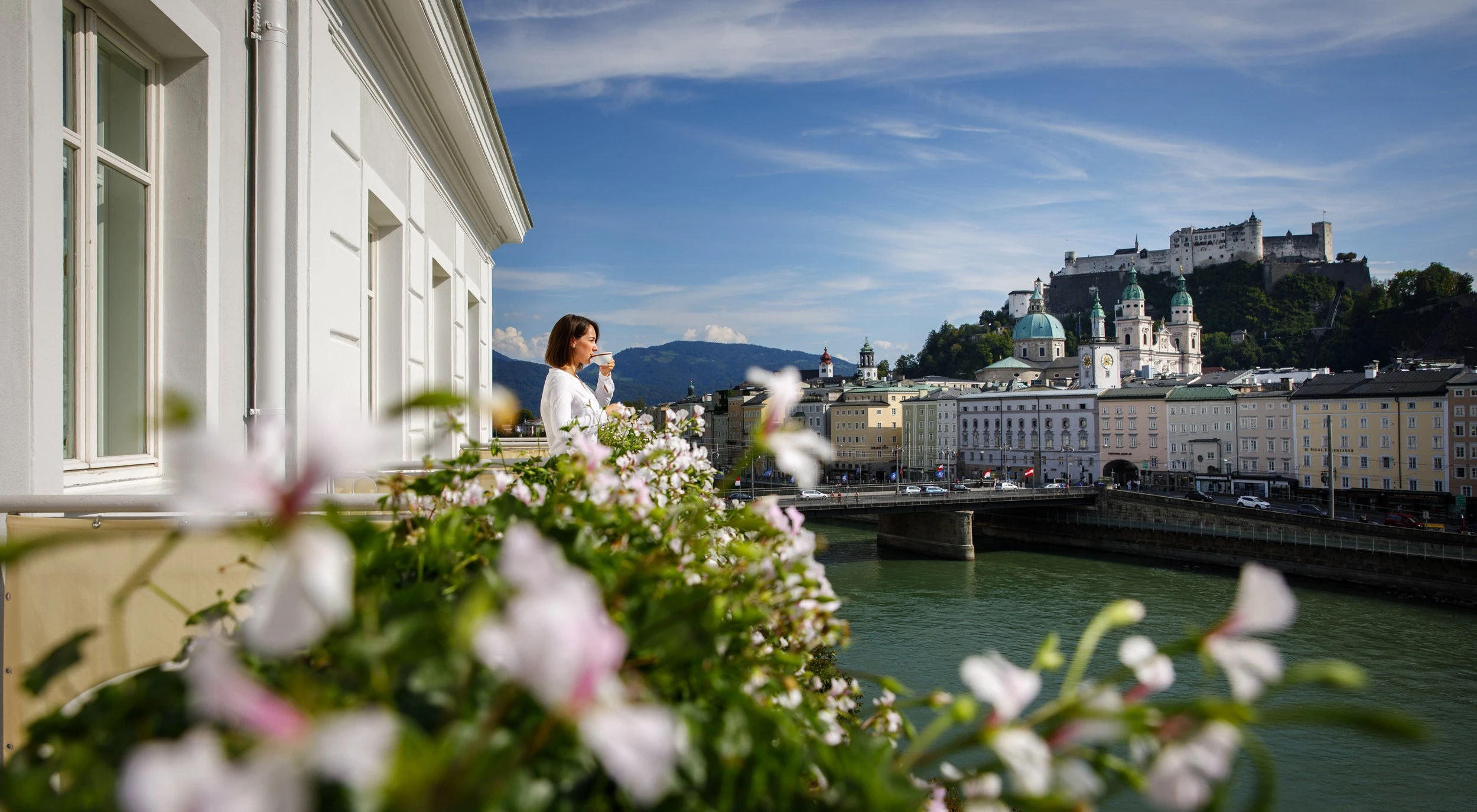 Woman enjoying a cup of coffee on a terrace at Hotel Sacher Salzburg, overlooking the city and Hohensalzburg Fortress.