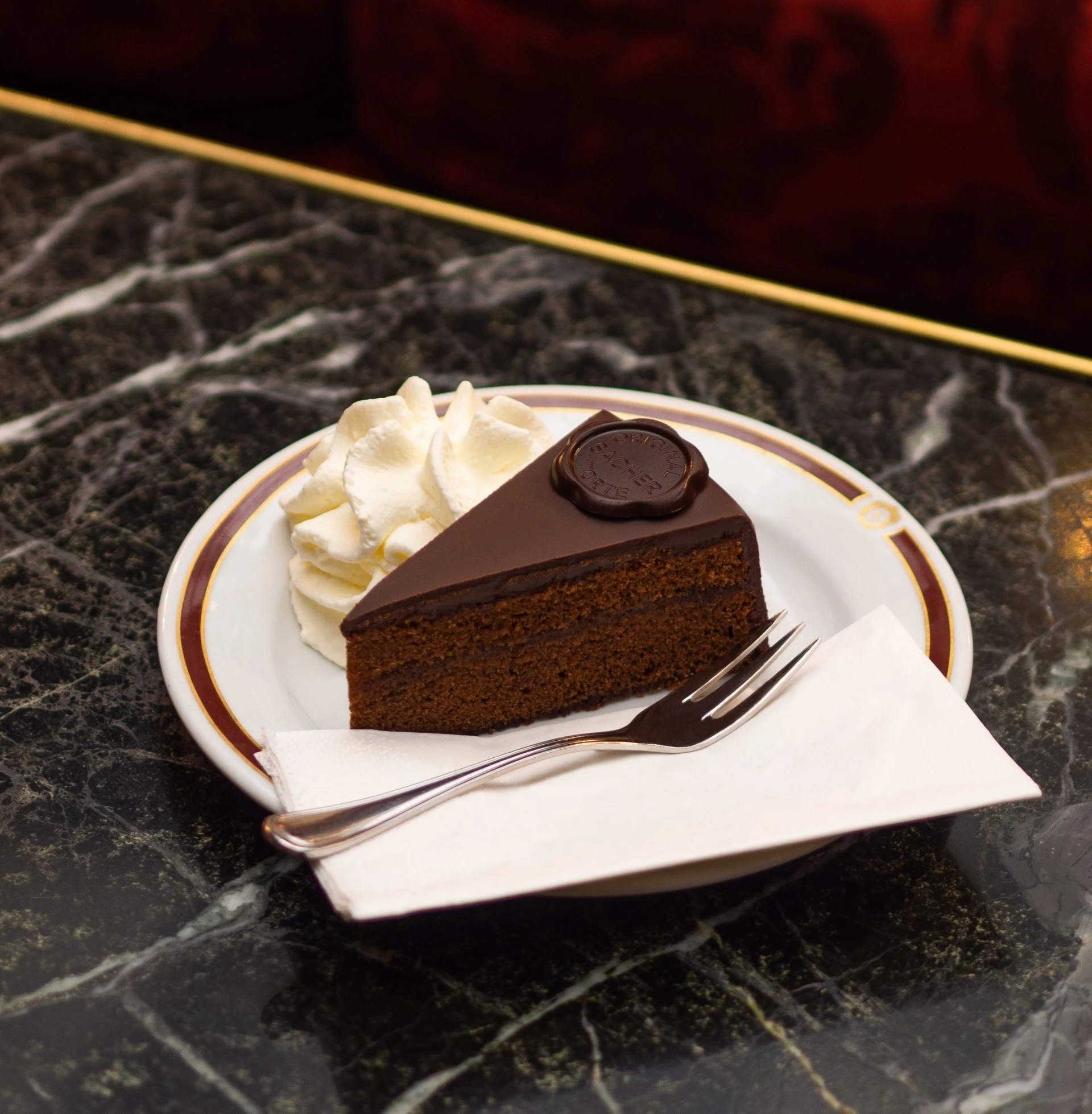 A slice of the Original Sacher-Torte, the famous chocolate cake, with cream on the side, served at Hotel Sacher.