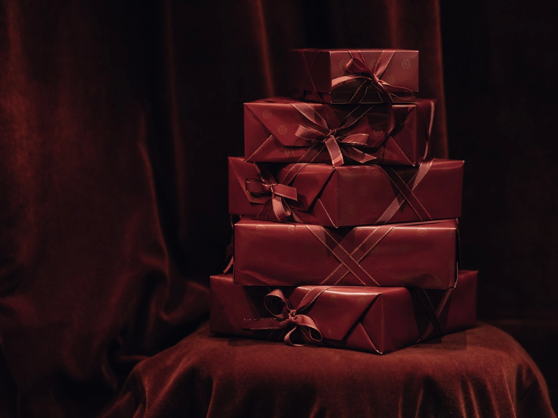 A luxurious stack of burgundy-wrapped Original Sacher-Torte boxes rests elegantly on a velvet-covered chair, ready to be gifted from Hotel Sacher Wien.