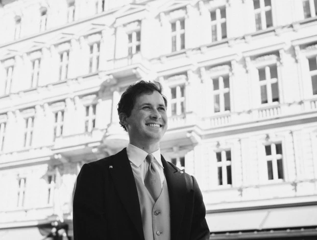 A sharply dressed doorman smiles warmly in front of the grand facade of Hotel Sacher Wien, welcoming guests with signature Viennese charm.