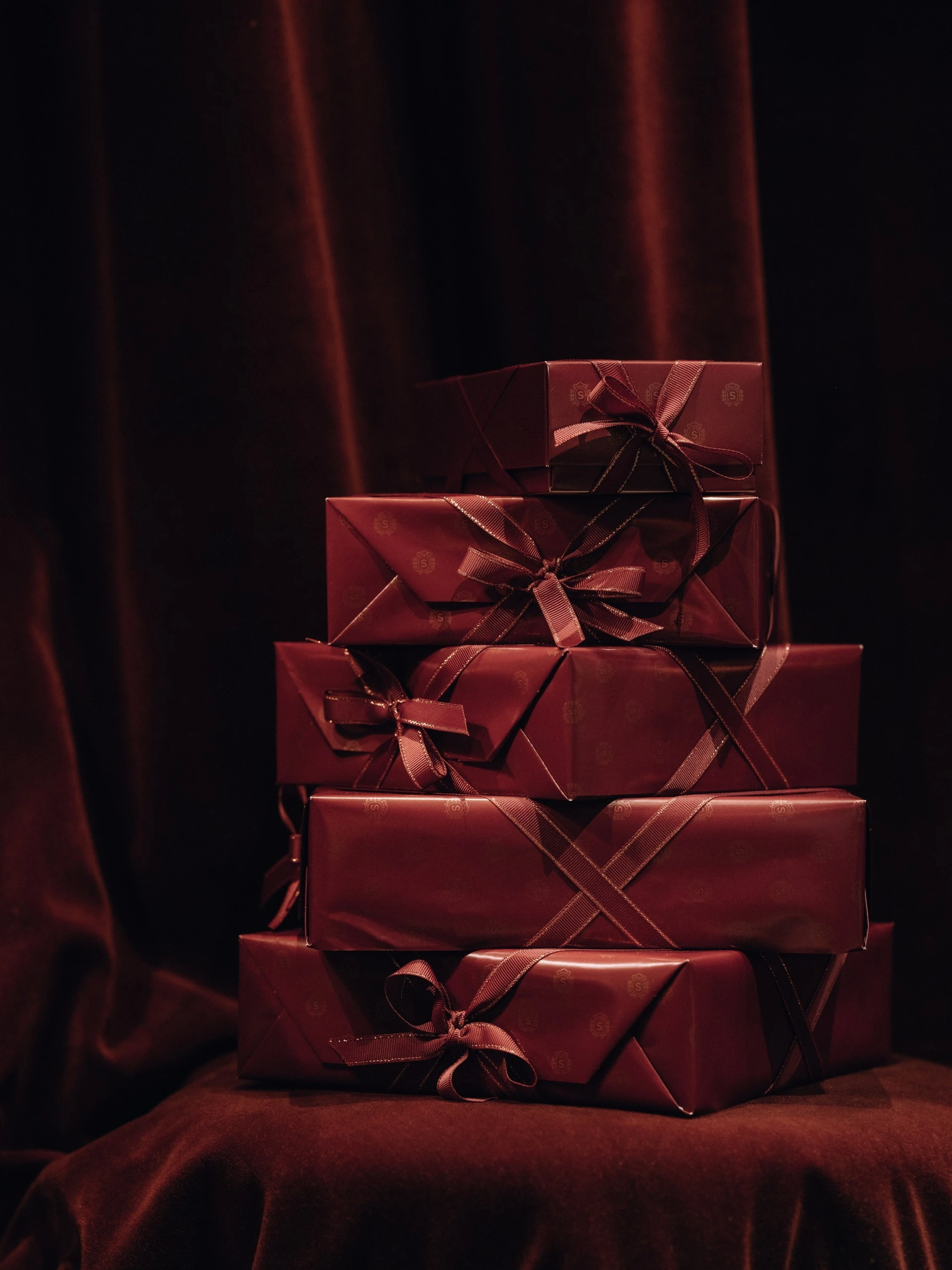 A dramatic display of stacked red gift boxes wrapped with ribbons, containing the Original Sacher-Torte, set against a rich velvet backdrop.