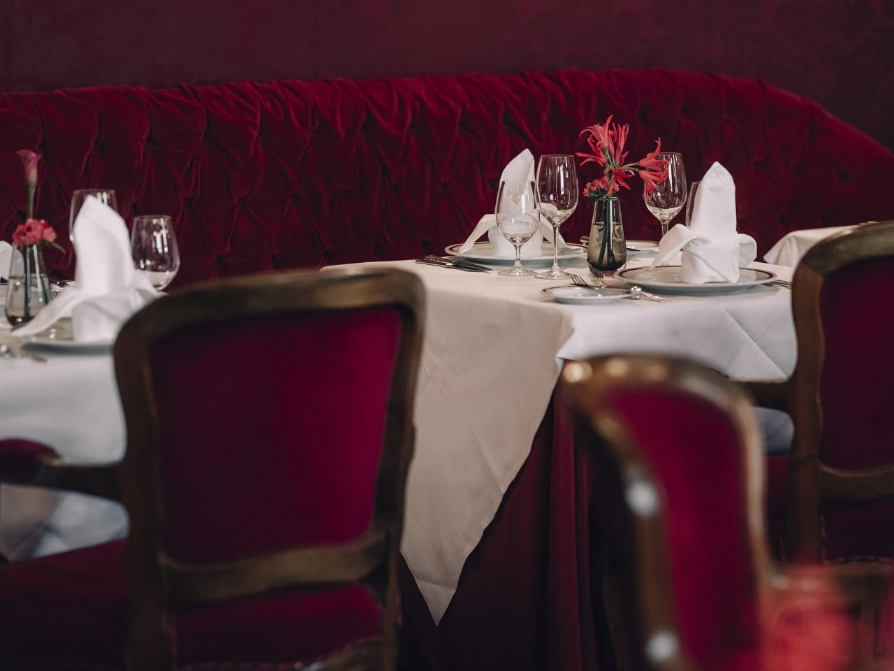 An elegantly set table with white linens, red velvet chairs, and a small floral centerpiece in Restaurant Rote Bar.