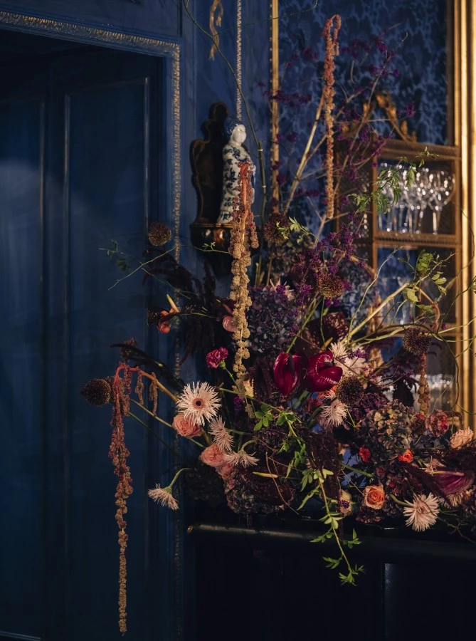 Hotel Sacher Architektur Wien-184_Web This image captures the dramatic elegance of the Blaue Bar, with its rich blue walls, golden accents, and a striking floral arrangement that adds a touch of wild beauty to the bar’s opulent and moody ambiance.