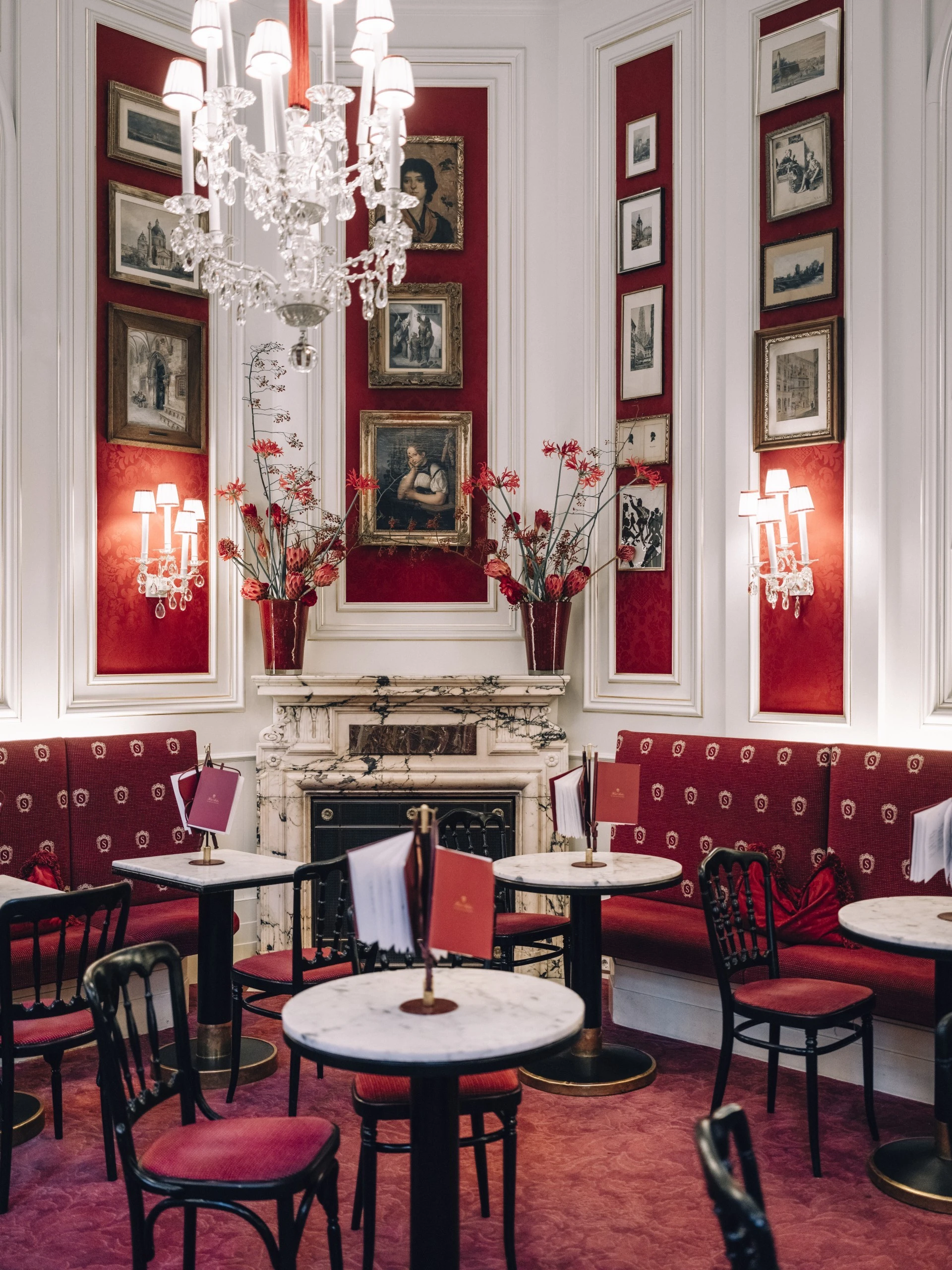This image showcases the iconic Café Sacher Wien, with its elegant red and white color scheme, marble-topped tables, classic Thonet chairs, crystal chandelier, and historic artwork creating a refined Viennese coffeehouse atmosphere steeped in tradition.