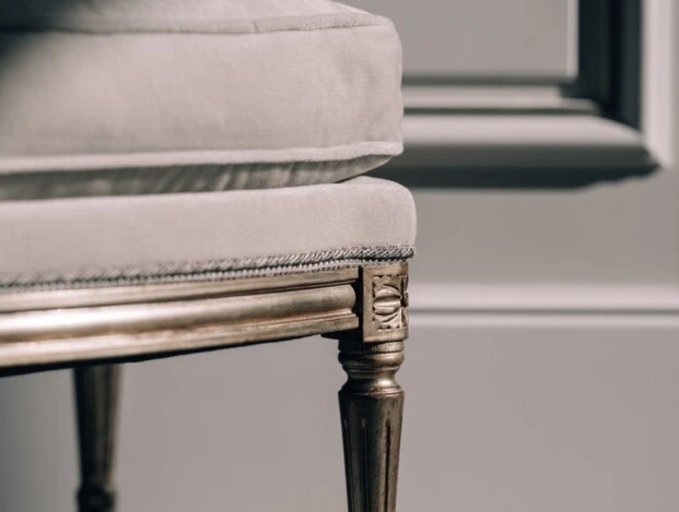 A close-up of an elegant, classic-style chair, highlighting its plush fabric and decorative gilded leg.
