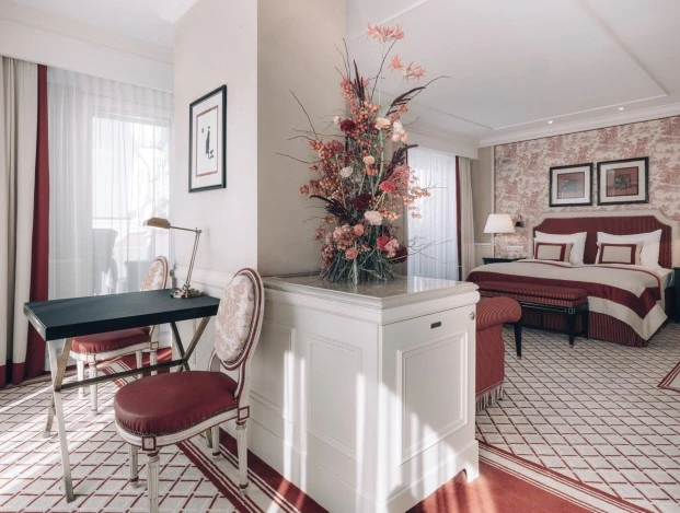 Suite at Hotel Sacher Wien, featuring a red and cream striped bed, a stylish desk, elegant chairs, and beautiful floral arrangements that create a warm and inviting atmosphere.