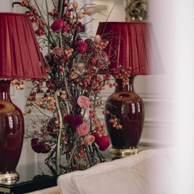 Bed with red and cream striped sheets, a nightstand with a lamp, and vintage floral wallpaper on the walls.