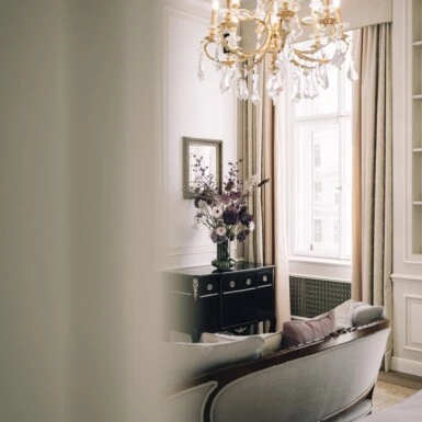 Grand Signature Suite at Hotel Sacher Wien, showcasing its luxurious and elegant decor. The room features refined design elements, such as a crystal chandelier, a stylish sofa, and a beautiful flower arrangement. This suite exemplifies the hotel's classic Viennese luxury, offering a perfect blend of sophistication and comfort.