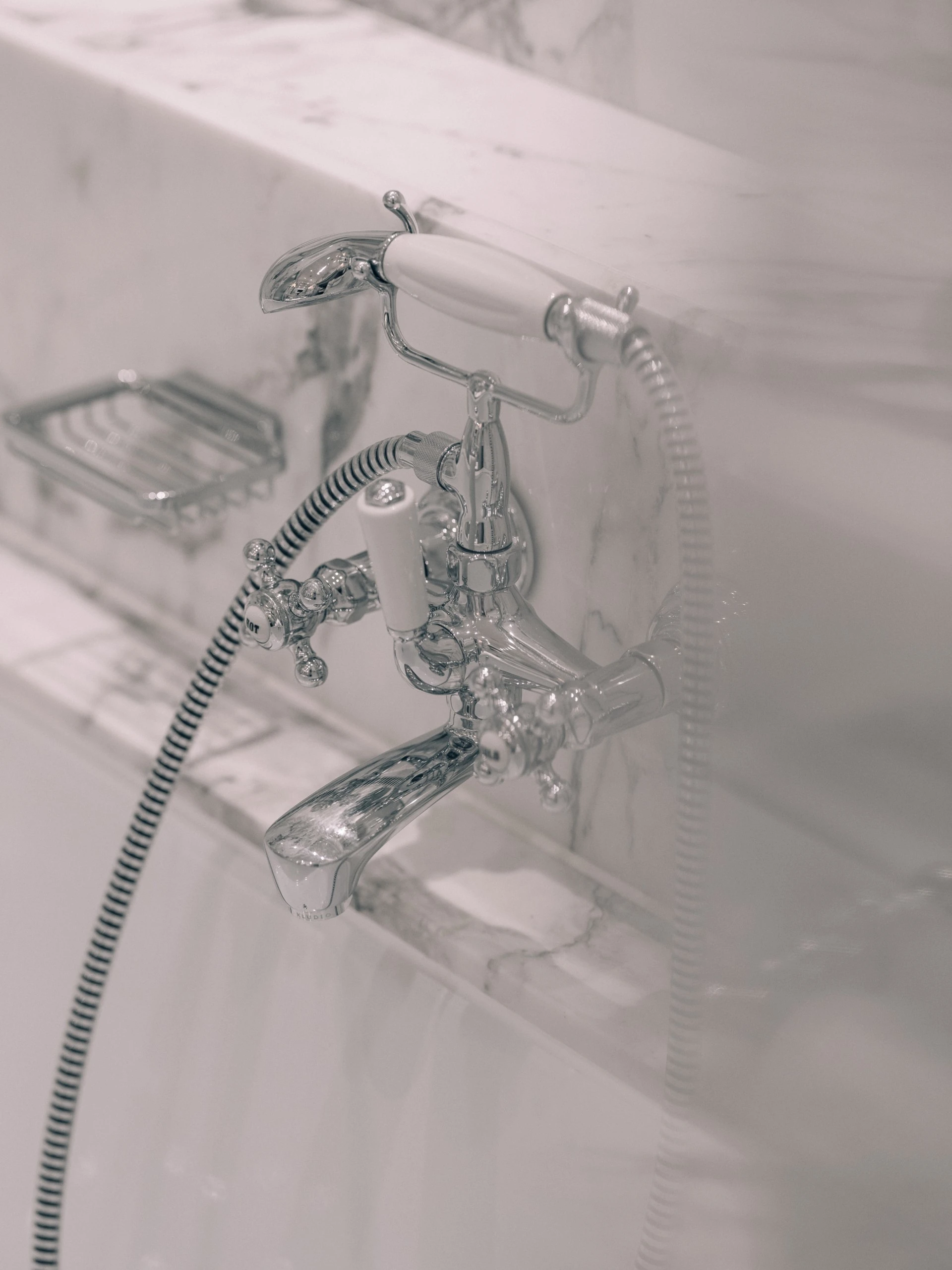 This is a close-up of an elegant silver bathtub faucet with a white handle, set against smooth white marble.