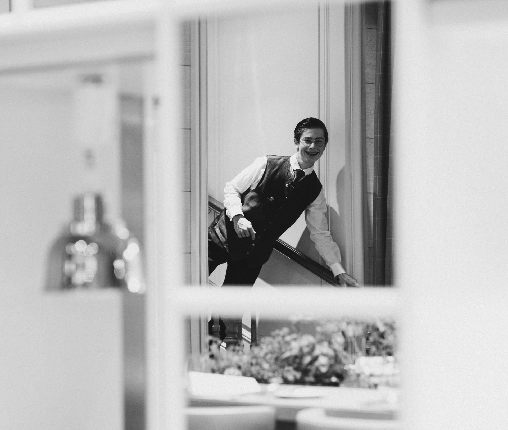 Captured in a mirror’s reflection at Hotel Sacher Salzburg, a cheerful staff member in formal attire descends a staircase with a warm smile, embodying the hotel’s signature elegance and hospitality.