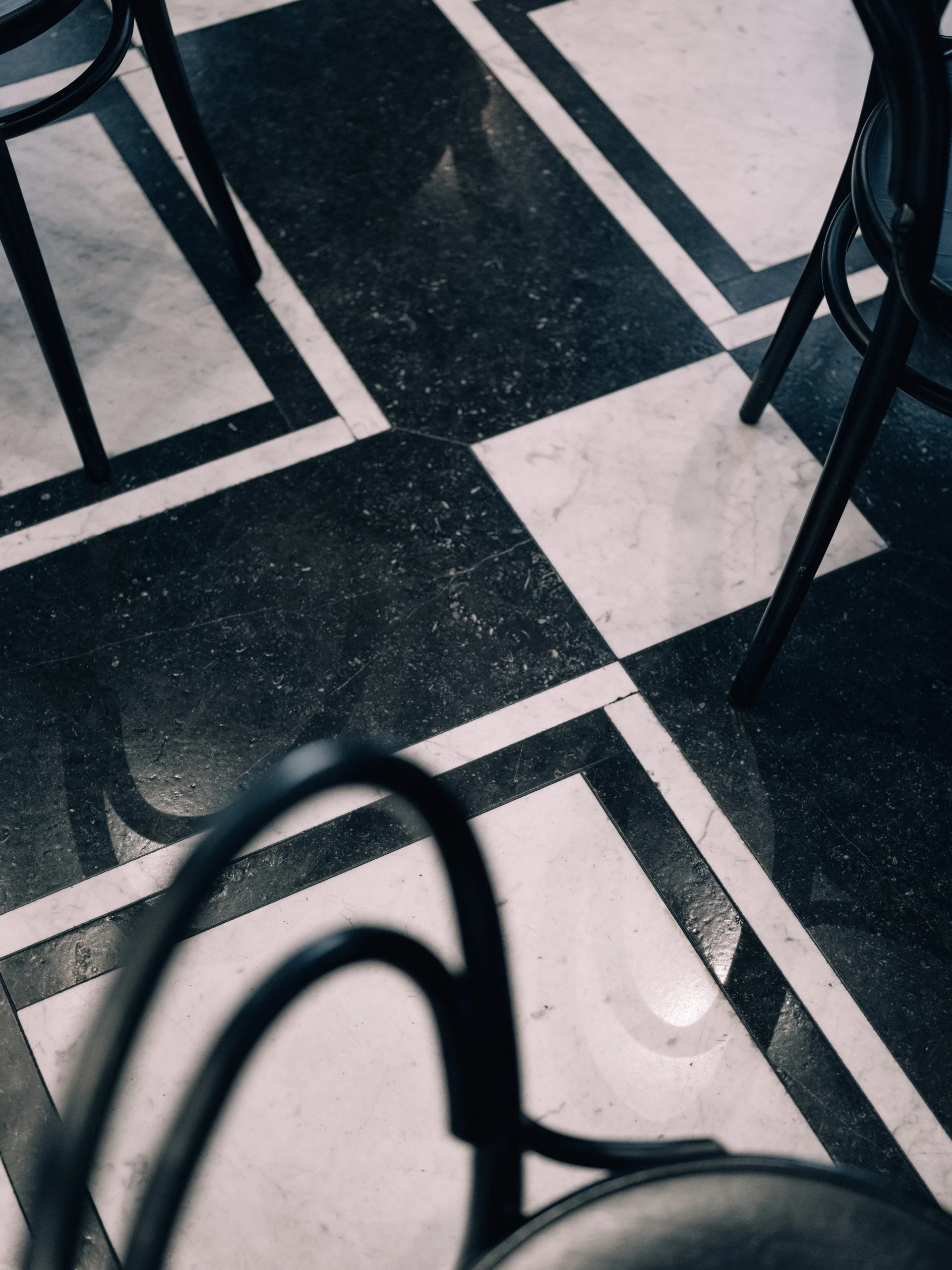 The image shows a close-up of black and white checkered marble flooring with elegant curved café chairs at Café Bel Etage Sacher, evoking a timeless, classic ambiance.