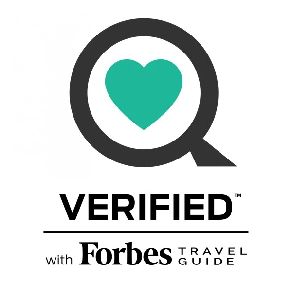 Logo mit schwarzem Kreis und türkisfarbenem Herz in der Mitte, darunter die Aufschrift „VERIFIED with Forbes Travel Guide“ auf weißem Hintergrund.