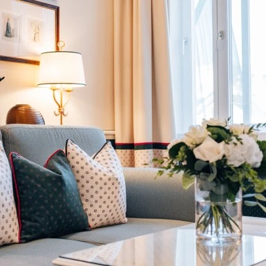 A cozy corner at Sacher Salzburg featuring patterned pillows, elegant curtains, and a fresh floral arrangement.