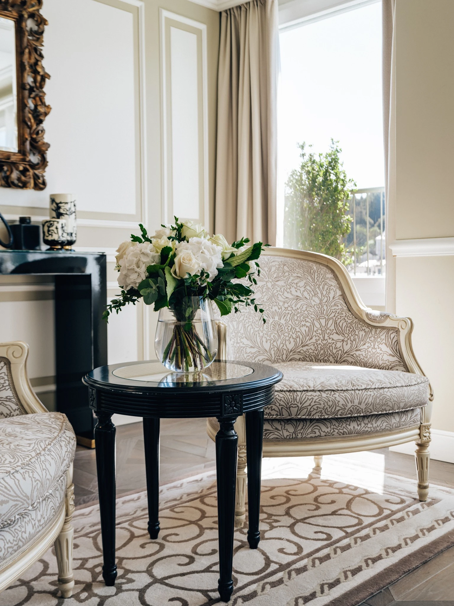 A bright and elegant seating nook at Hotel Sacher Salzburg features classic armchairs, a fresh bouquet of white flowers, and refined decor bathed in natural light.