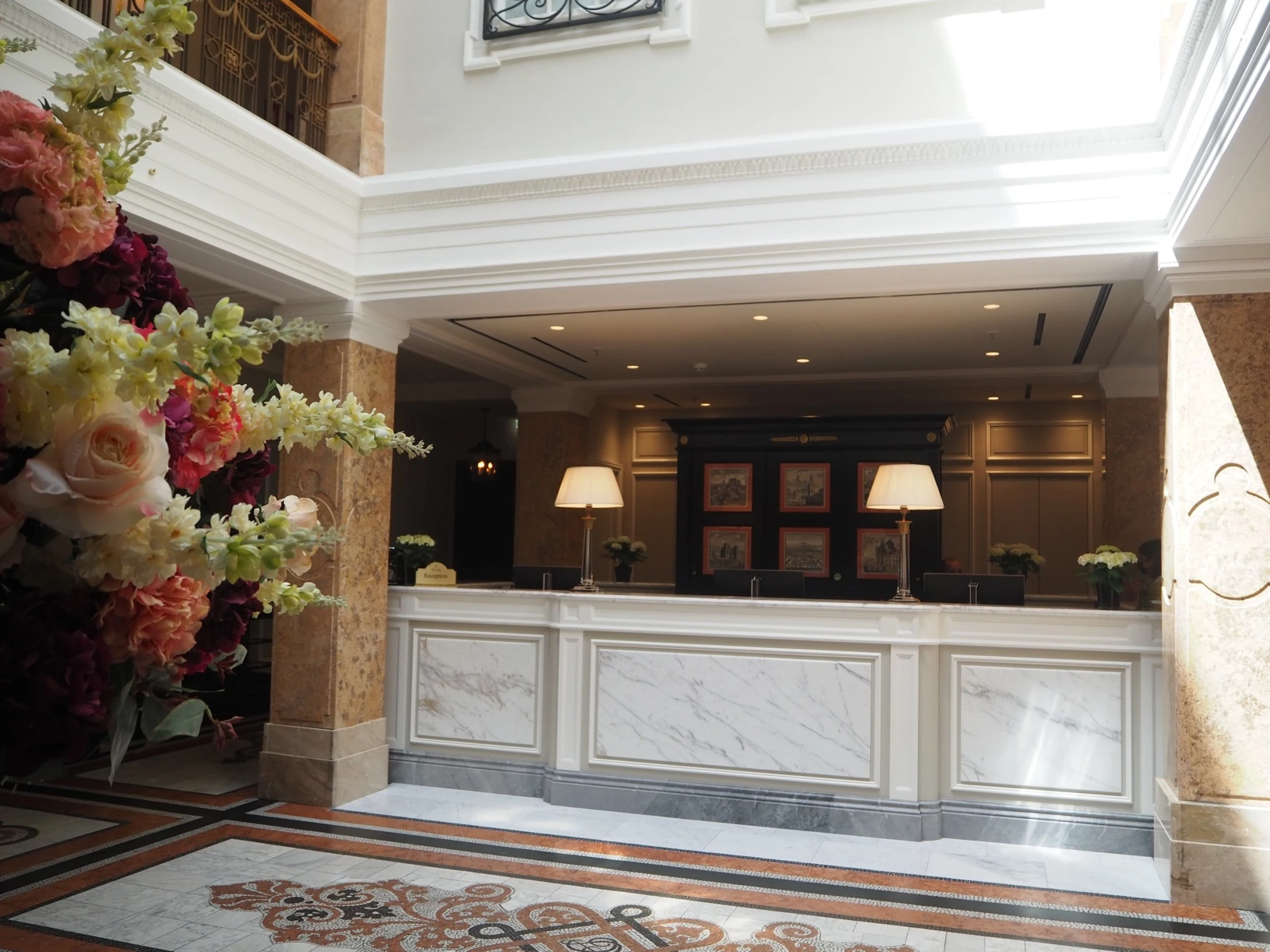 The photo captures the elegant reception area of Hotel Sacher Salzburg, featuring a marble-front desk, warm lighting, and a stunning floral arrangement that exudes timeless luxury.