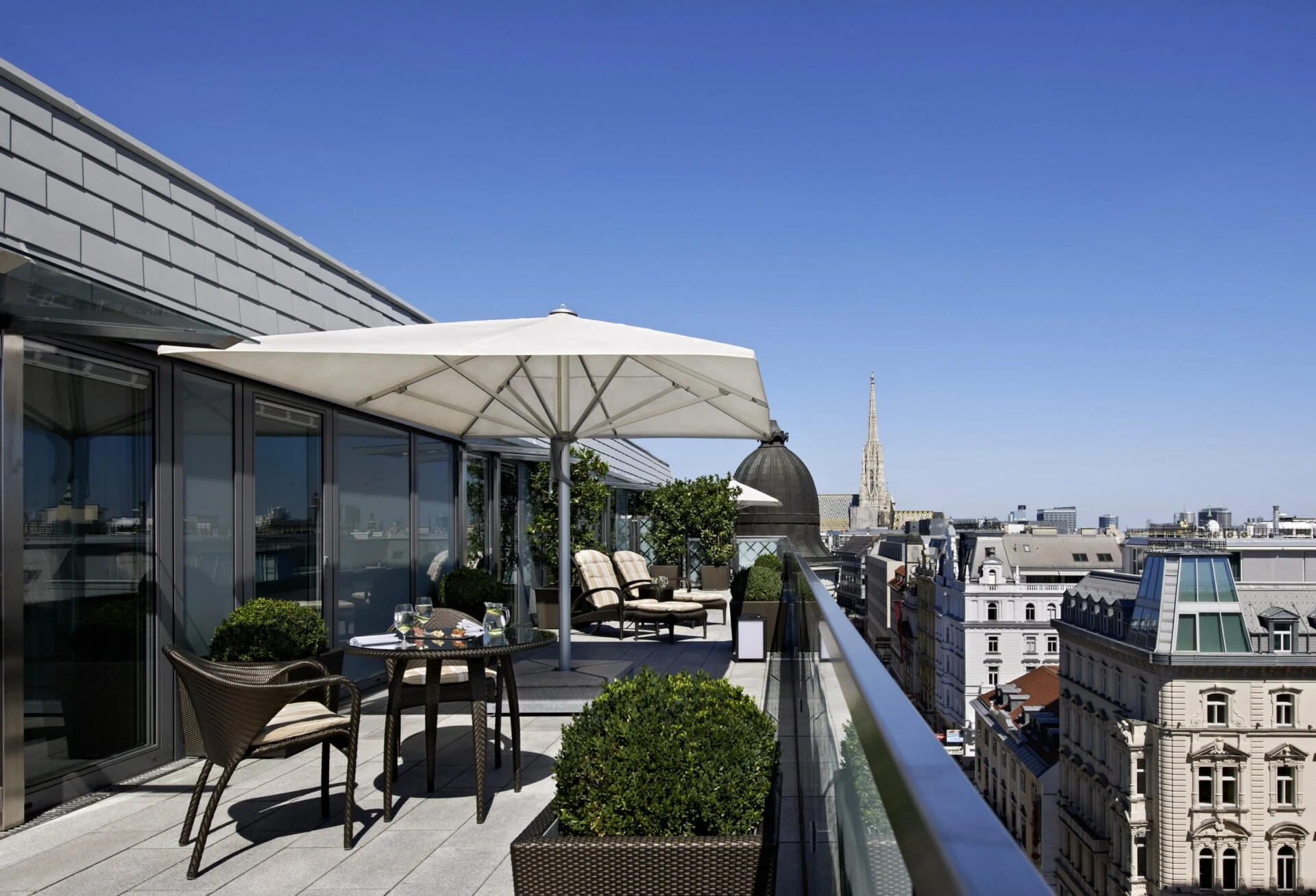 View from the Grand Signature Penthouse Suite at Hotel Sacher, showcasing the spacious rooftop terrace with comfortable seating, perfect for enjoying the panoramic views of Vienna, including a glimpse of the famous St. Stephen's Cathedral.