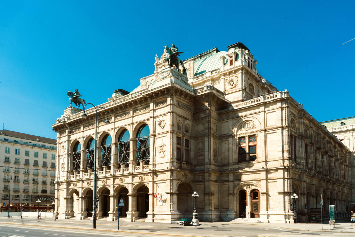 Vienna State Opera building: Grand, ornate facade of the opera house in Vienna under a clear blue sky, with architectural details and statues visible.