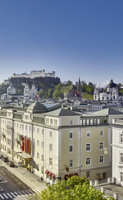 Panoramic view of Hotel Sacher Salzburg with Hohensalzburg Fortress, historic rooftops, and mountains in the background