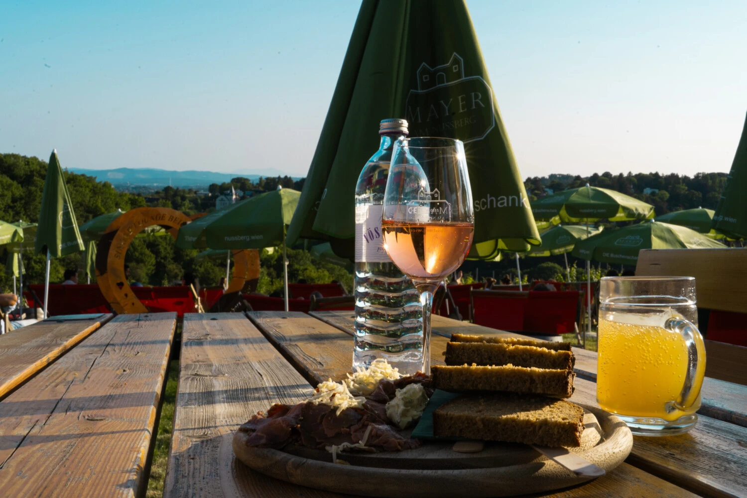 A rustic table with a glas of rose, sturm and a wooden board with roast beef and dark bread.