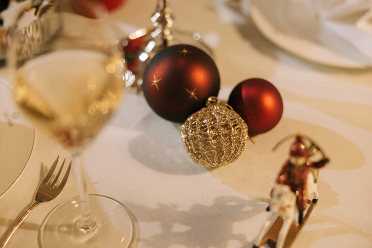 A close-up of a festive table with two red and one gold Christmas baubles, a ski ornament, and a wine glass.