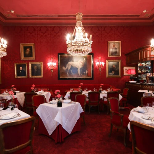 The Rote Bar offers elegant dining surrounded by red velvet, chandeliers, and imperial portraits.