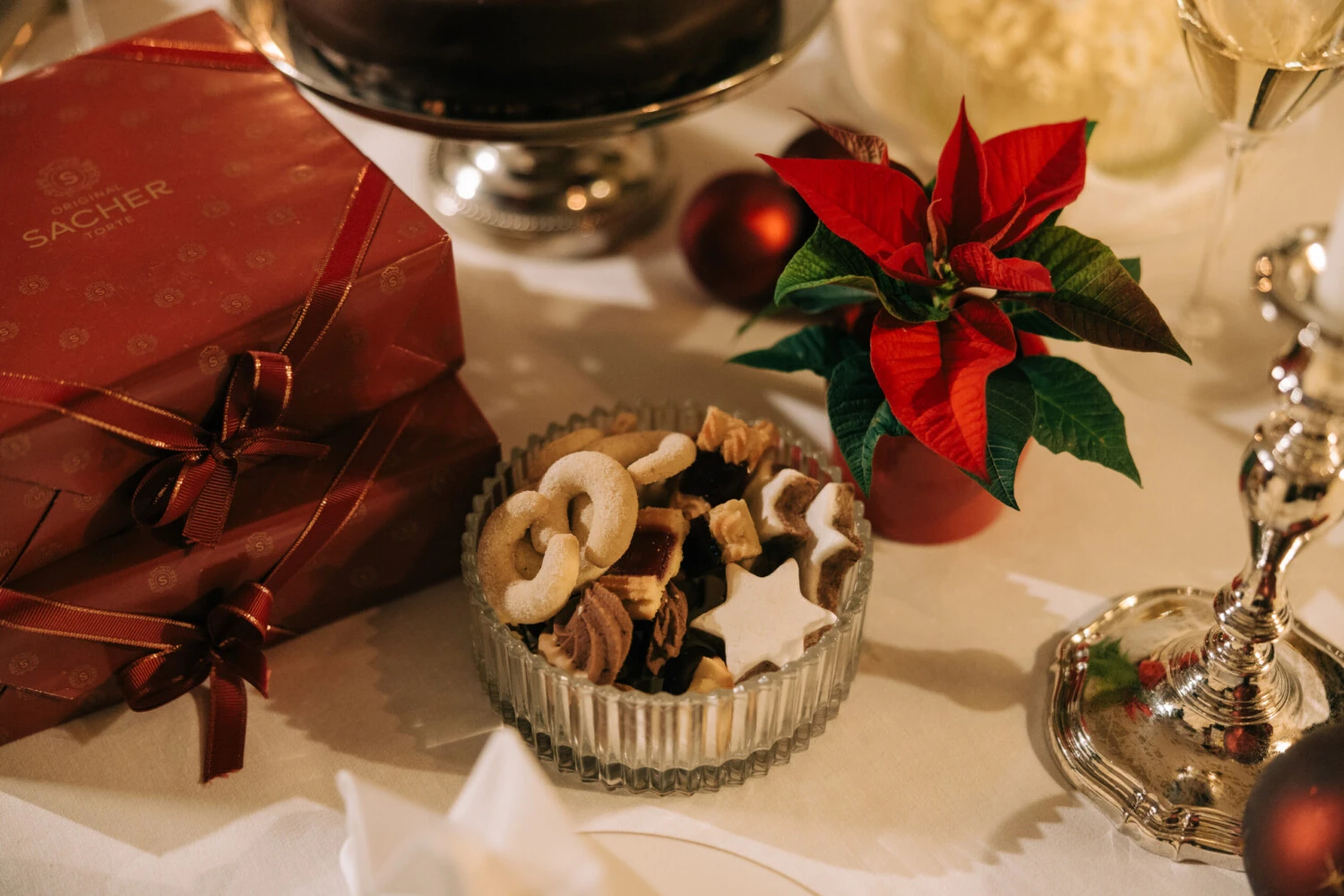 A festive table setting with traditional Austrian Christmas cookies, a red poinsettia, and a Original Sacher-Torte gift box.