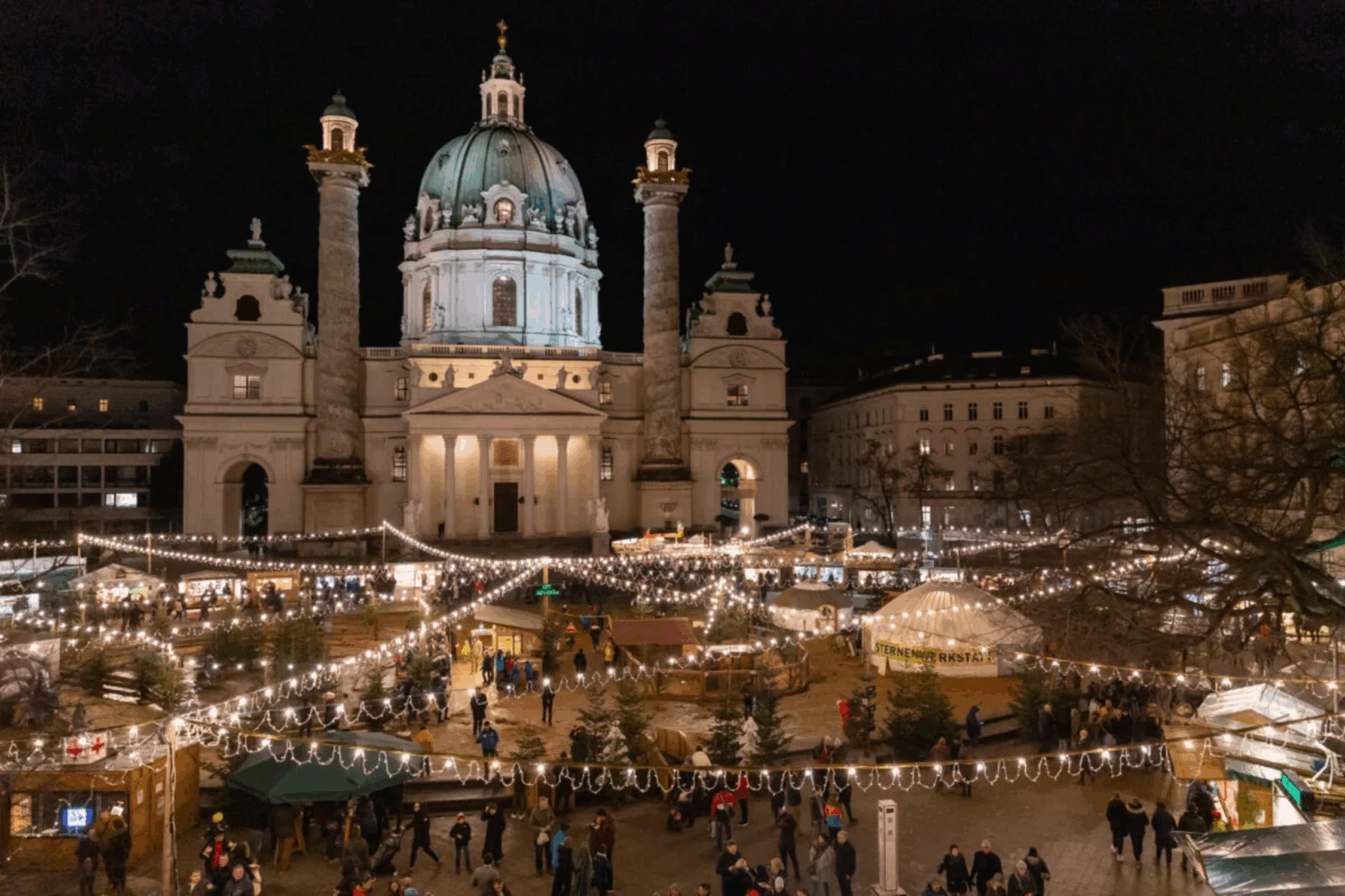 The Karlsplatz Christmas market in Vienna at night, with the illuminated Karlskirche (St. Charles Church) in the background.