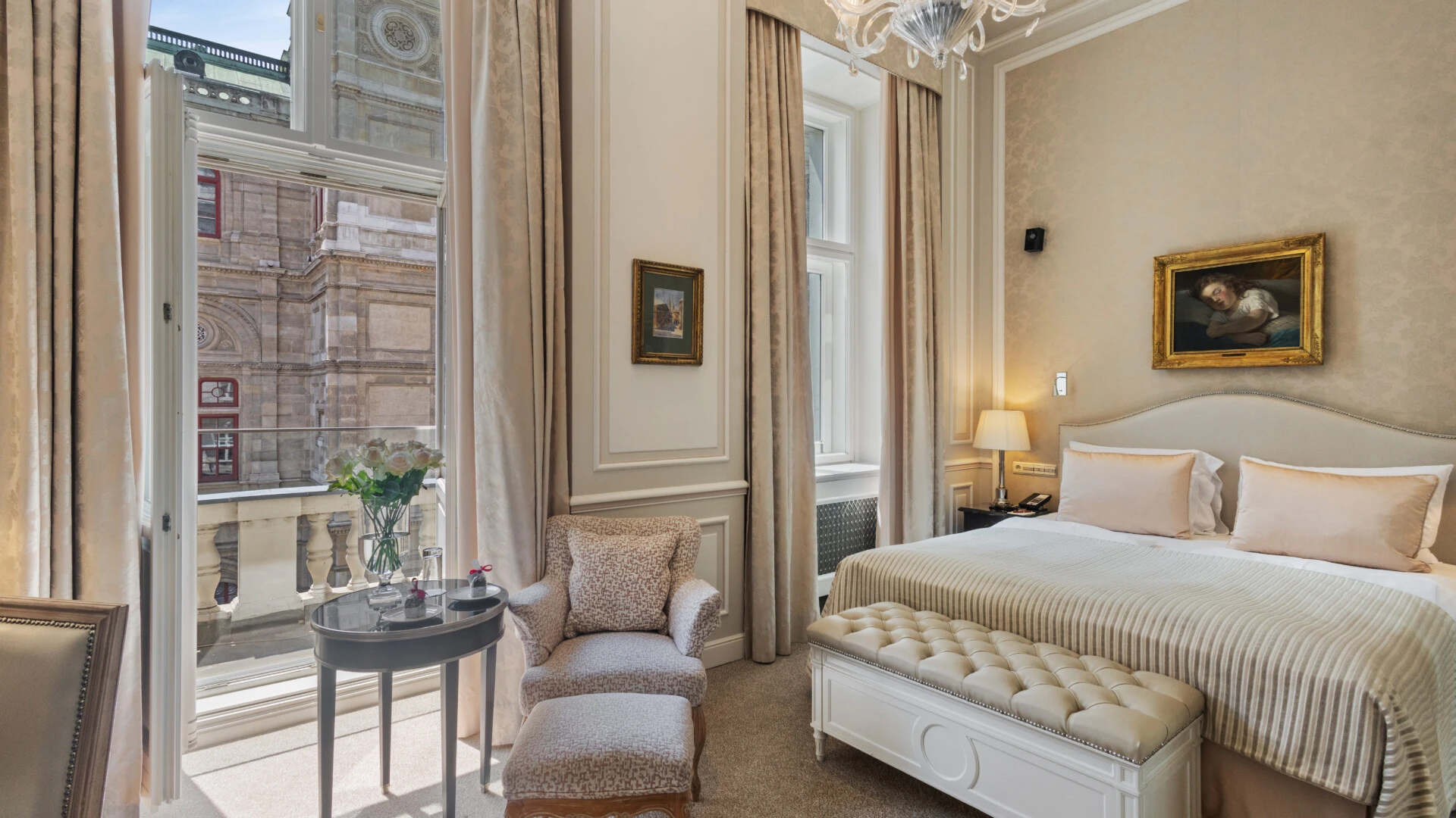 A beautiful hotel room featuring a bed, elegant furnishings, and a stunning balcony view of the Vienna State Opera (Wiener Staatsoper).