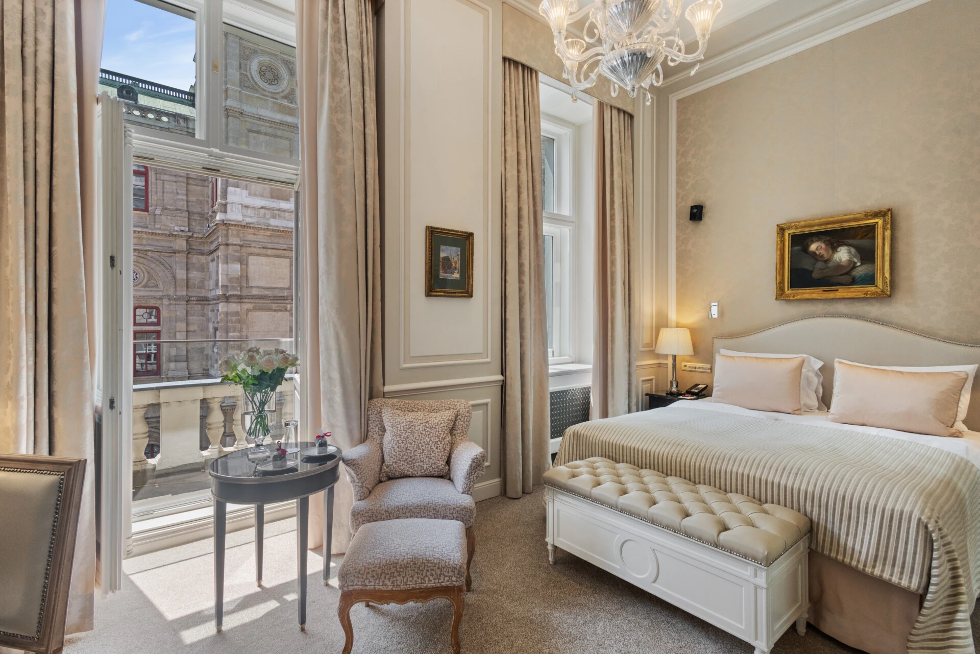 A beautiful hotel room featuring a bed, elegant furnishings, and a stunning balcony view of the Vienna State Opera (Wiener Staatsoper).