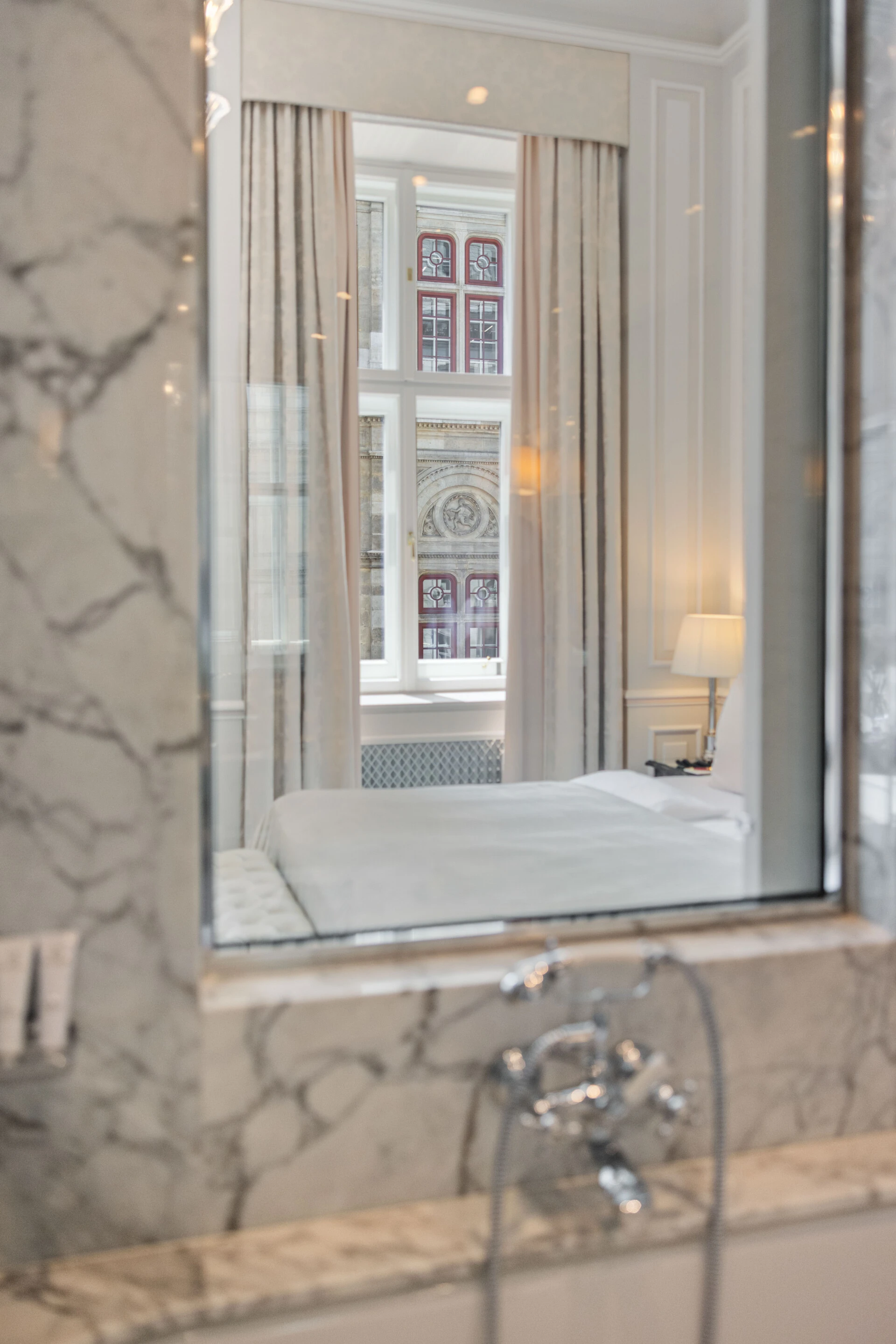A creative shot showing the reflection of a hotel room and its stunning view of the Vienna State Opera in a marble bathroom mirror.