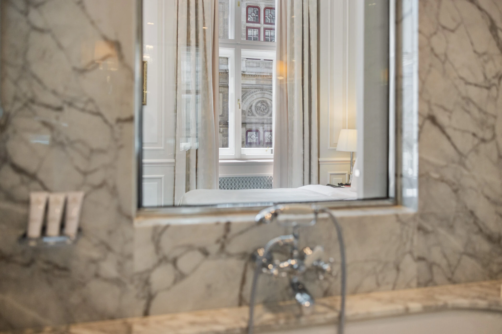 A creative shot showing the reflection of a hotel room and its stunning view of the Vienna State Opera in a marble bathroom mirror.